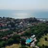Vista aerea di un borgo costiero con edifici, campi e mare sullo sfondo.