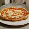Pizza margherita su un piatto bianco appoggiato su un tavolo di marmo.
