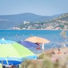 Spiaggia con ombrelloni colorati e bagnanti, mare azzurro e colline sullo sfondo.