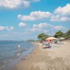 Una spiaggia con sabbia, mare calmo e ombrelloni colorati sotto un cielo azzurro.