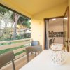 Balcone soleggiato con tavolo bianco e sedie, vista su giardino alberato, porta aperta su cucina.