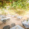 Giardino di un ristorante con tavoli apparecchiati sotto un pergolato ricoperto di foglie.