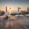 Terrazza in legno con lettini e ombrelloni, vista mare al tramonto.