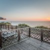Terrazza in legno con sedie e ombrelloni, vista mare al tramonto.
