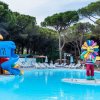 Una piscina con scivolo blu e rosso, e una statua colorata al centro. Alberi sullo sfondo.