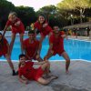 Sei persone in abiti rossi posano in un gruppo gioioso vicino a una piscina.