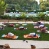 Persone che fanno yoga su tappetini colorati su un prato vicino a una piscina.