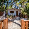 Una casa bianca con staccionata in legno, circondata da alberi, con un barbecue esterno.