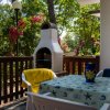 Un patio con tavolo, sedie e barbecue, circondato da fiori rosa e alberi.