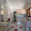 Cucina con tavolo da pranzo, sedie bianche e pensili beige. Pavimento bianco con piastrelle rosse.