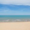 Spiaggia di sabbia fine con mare calmo e cielo azzurro.