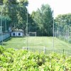 Campo da calcio recintato circondato da alberi e cespugli verdi.