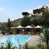 Piscina esterna con persone, circondata da alberi e gazebo.