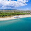 Spiaggia con lettini e ombrelloni e mare azzurro. Vegetazione e colline sullo sfondo.
