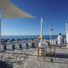 Terrazza con pavimento a mosaico affacciata su una spiaggia con ombrelloni blu.