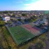 Un campo sportivo con campi da calcetto e tennis, circondato da edifici e verde.