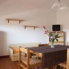 Sala da pranzo con tavolo in legno, fiori in vaso, frigo bianco e televisore su mobile.