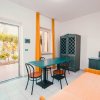 Area soggiorno con tavolo blu, sedie nere, armadio, letto singolo e porte aperte su giardino.