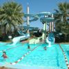 Piscina con scivoli d'acqua e ragazzi che nuotano, circondata da palme.