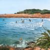 Spiaggia sabbiosa con persone che nuotano in una baia.