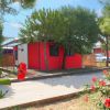 Casa rossa con recinzione in legno circondata da alberi e fiori rossi.
