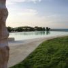 Piscina vista mare, contornata da prato verde e ombrelloni bianchi.