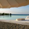 Piscina a sfioro vicino alla riva, con ombrellone beige e sabbia.