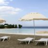 Due lettini bianchi sotto ombrelloni beige vicino a una piscina con vista mare.