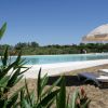 Lettini sotto un ombrellone beige accanto a una piscina, con piante in primo piano.