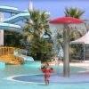 Bambina con braccioli in piscina, sotto un fungo a pioggia, vicino a scivoli d'acqua e palme.