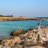 Bicicletta bianca parcheggiata su rocce vicino a una baia con acqua turchese.