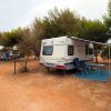Camper parcheggiato su terreno arido, circondato da alberi e sedie pieghevoli sotto una tenda.