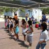 Persone in fila sotto una tettoia, su una superficie scoperta. Sembrano ascoltare istruzioni.
