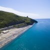 Spiaggia rocciosa e mare blu vicino a una collina verde.