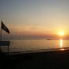 Spiaggia al tramonto con bandiera nera su un palo e mare calmo.