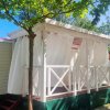 Un bungalow bianco con tende su una veranda, circondato da alberi.