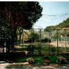 Campo sportivo recintato circondato da alberi e fiori colorati.