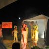 Ragazzi in scena con bigodini colorati, su un palco con il logo 
