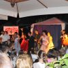 Persone in costume che ballano e cantano sul palco di un musical, con pubblico seduto.
