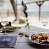 Tavola apparecchiata con piatti di pesce e mare sullo sfondo.